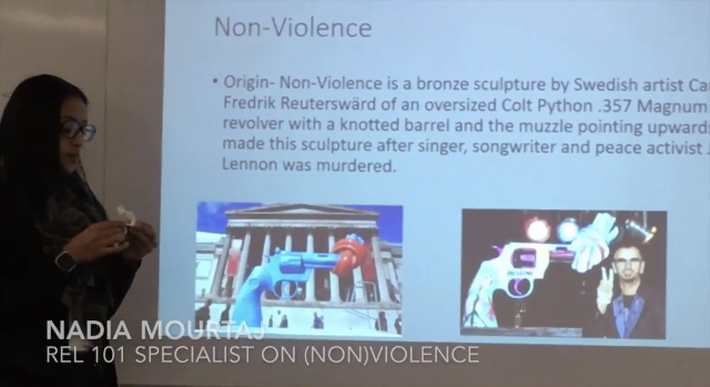Nadia Mourtaj giving a presentation on Non-violence. She's standing in front of Reutersward's Colty Python .357 Magnum sculpture with the twisted barrel.