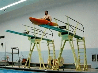 Man on a Kayak launching off of a diving board into a pool and falling flat on his face.