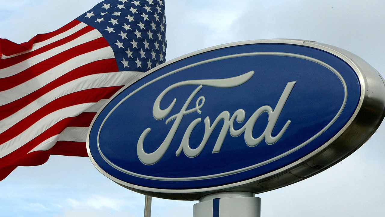 The Ford Motor Company logo next to an American Flag wavering.