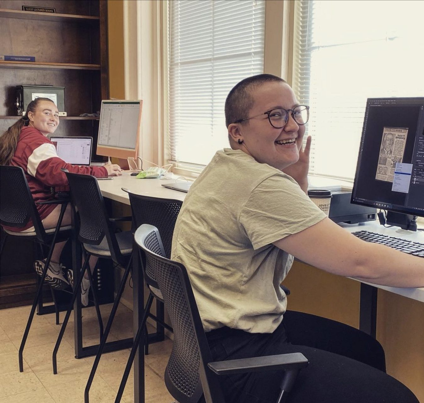 Two students are working on terminals of scanned newspaper clippings. They are smiling into the camera.