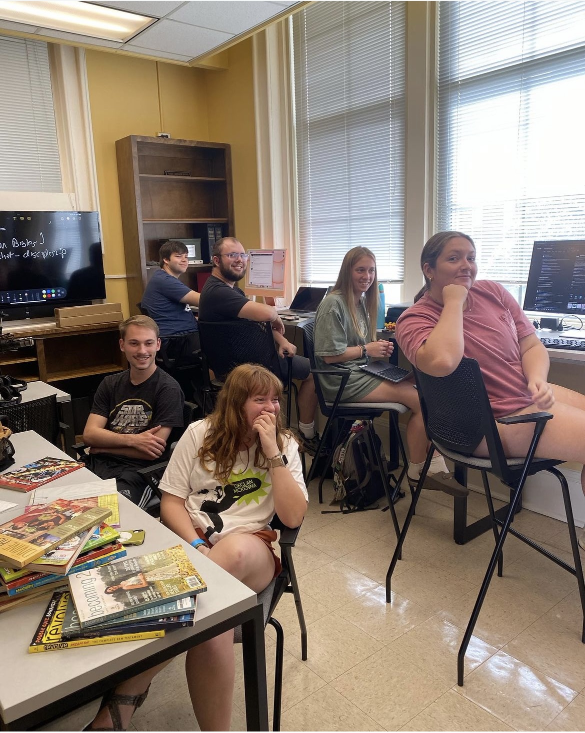 Students are looking into the camera as they work in front of computer consuls and stacks of BIblezines.