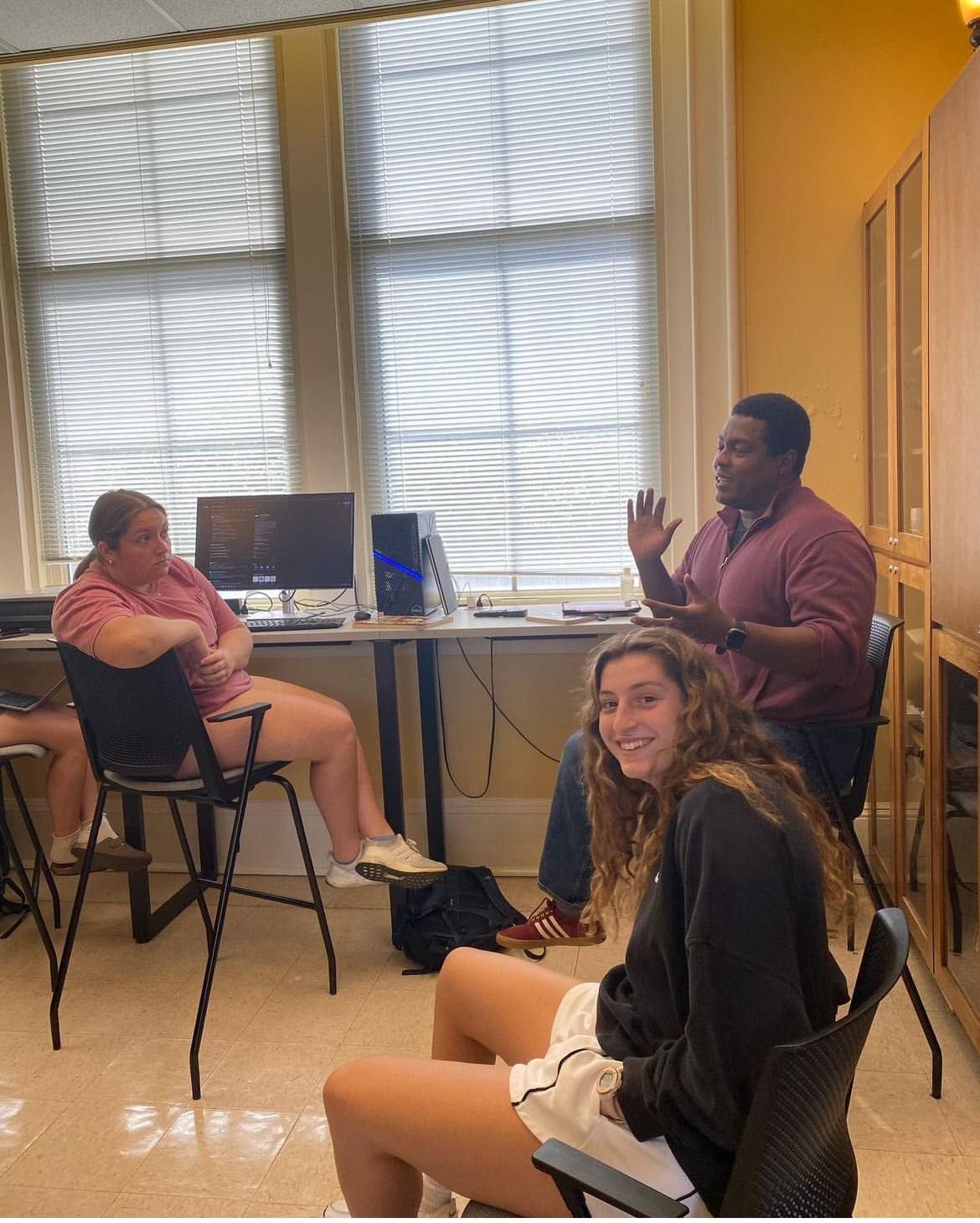 Students are paying attention to Dr. Newton speaking . One is looking at the camera smiling.
