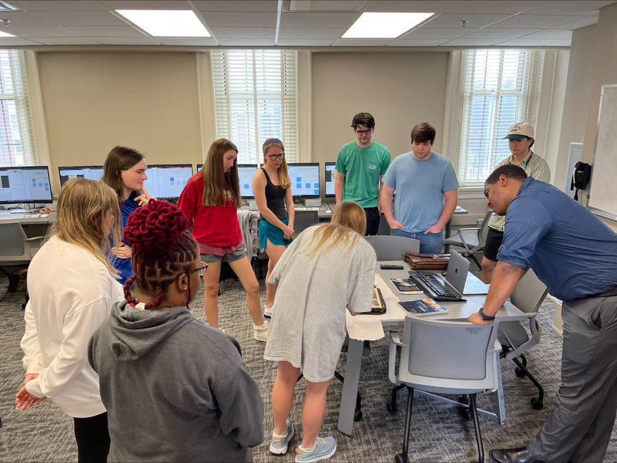 Dr. Newton is teaching a circle of students who are looking at a scrapbook.