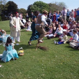 A picture of people gathered around a couple jumping the broom.