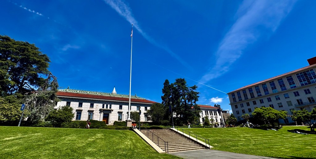Campus of Berkeley. There’s a photo of lawn with steps leading up to buildings in the California style.